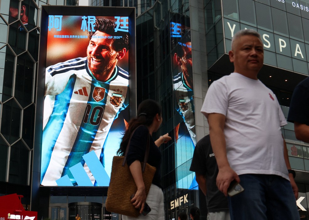 Pessoas caminham em frente a um enorme telão publicitário em Pequim com a foto de Lionel Messi — Foto: Maxim Shemetov/Reuters
